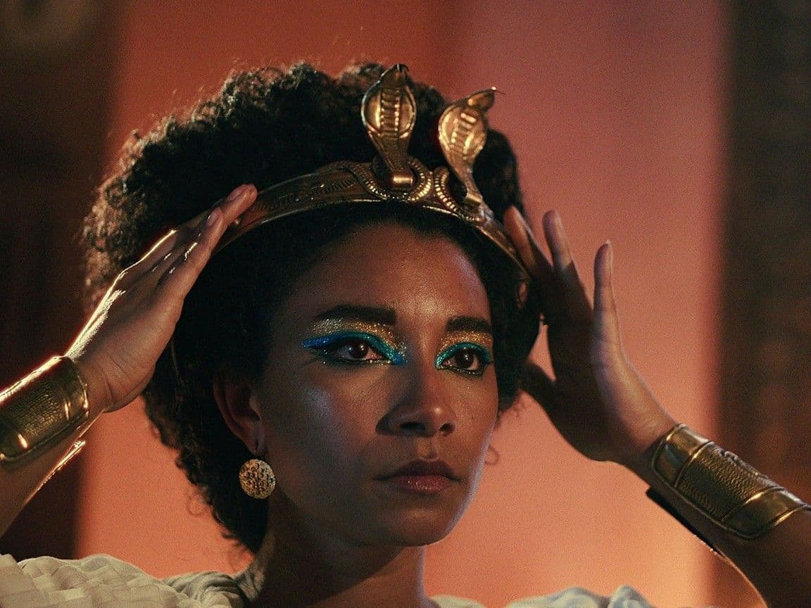 An image of a womans's head with her arms clutching an ancient Egyptian crown on her head