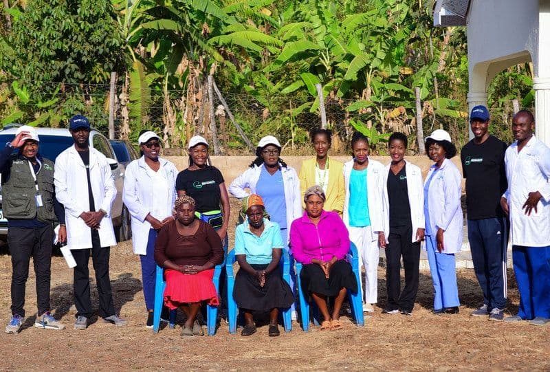 A photo with people posing for a picture. 11 are standing, while three others are seated in front of them, with some donning nursing uniforms.