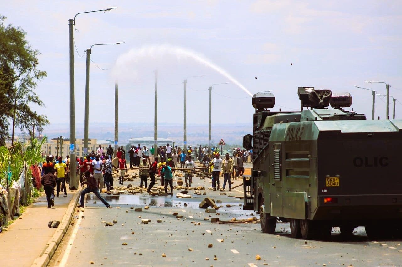 View of a police water canon spraying water on protestors who have barricaded the road with stones